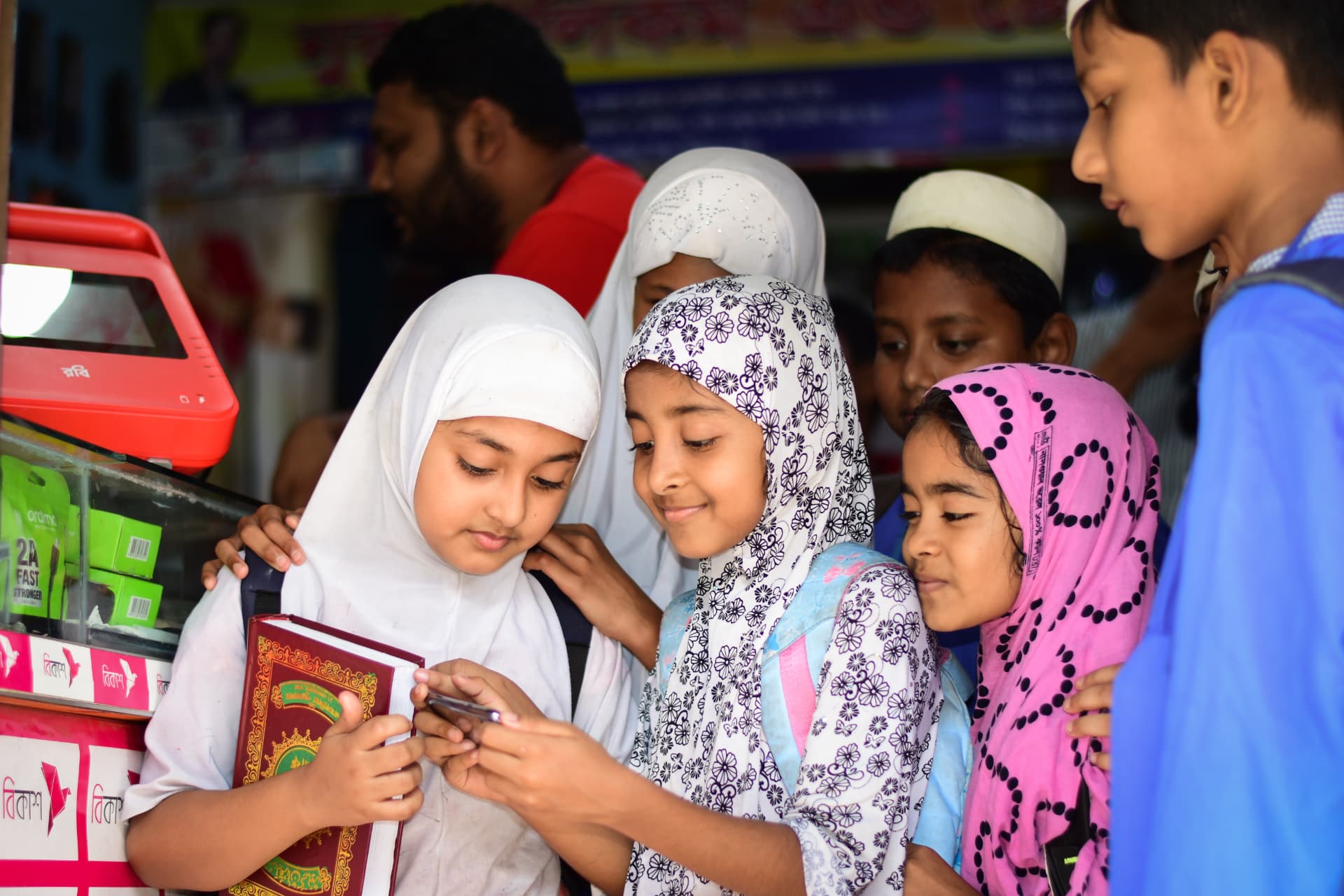 Children gathered around a smartphone at a shop counter beside a red BuffaloGrid hub