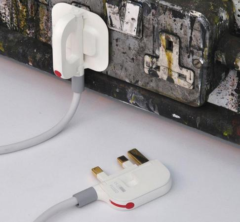 Two Mu folding plugs with cables in a workshop, one plugged into a worn industrial UK power strip and one resting with its pins facing up