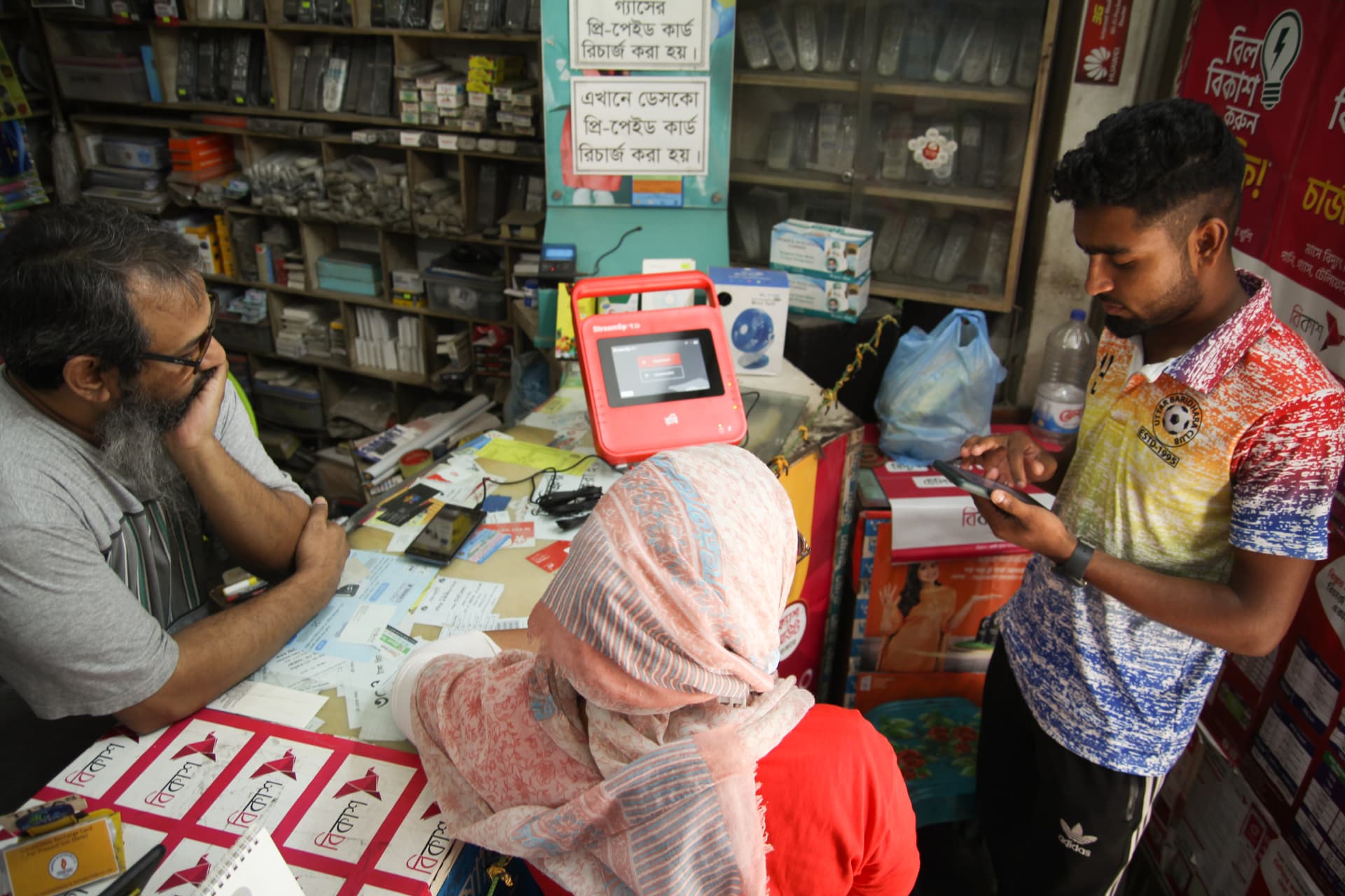 Customers and a shopkeeper around a red BuffaloGrid hub, with a customer using a smartphone