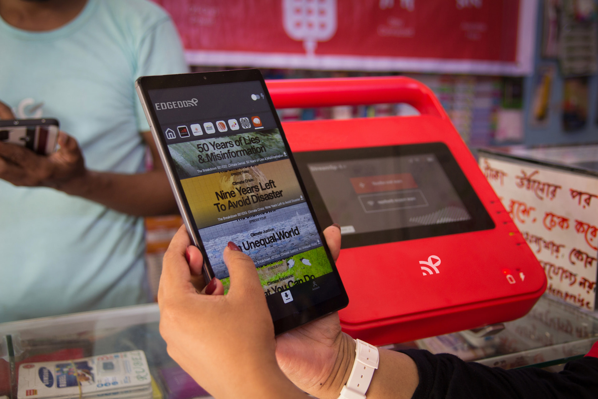 Hands holding a tablet showing an offline video app beside a red BuffaloGrid hub on a shop counter